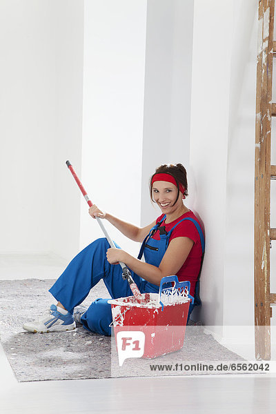 Young woman sitting with paint tin and paint brush  smiling  portrait