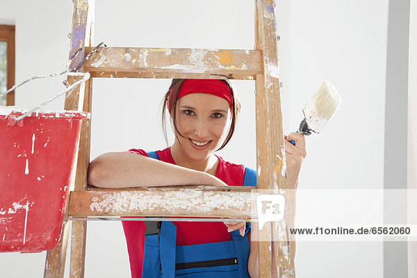 Young woman standing on step ladder with paint brush