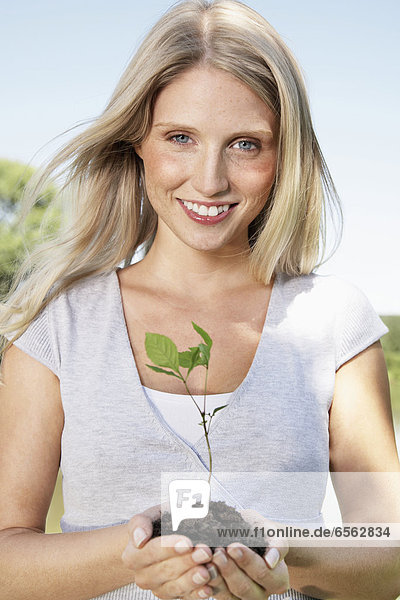 Young woman holding seedling  smiling  portrait