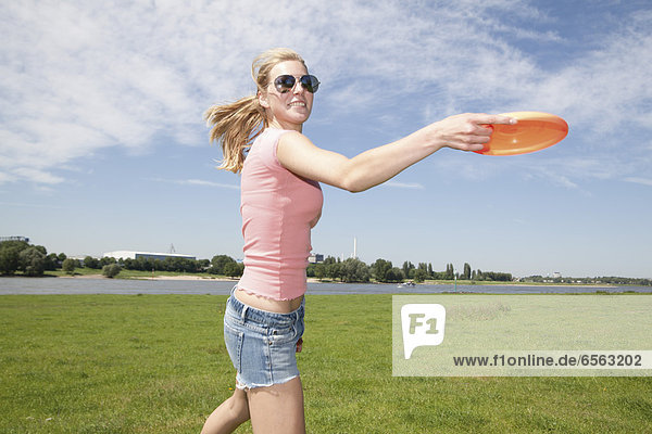 Germany  North Rhine Westphalia  Duesseldorf  Young woman playing with frisbee  smiling