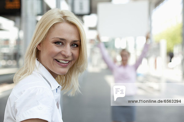Geschäftsfrau lächelnd  eine andere Frau mit Plakat im Hintergrund