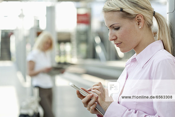 Frau mit Smartphone  Geschäftsfrau beim Zeitungslesen im Hintergrund