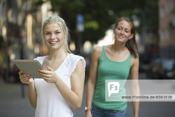 Germany  North Rhine Westphalia  Cologne  Young women with digital tablet on street  smiling