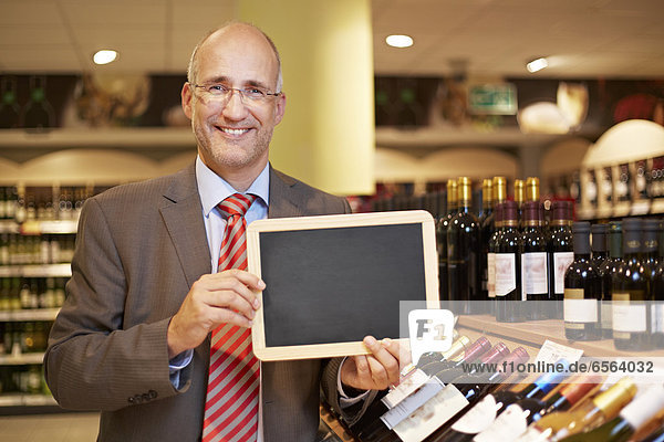 Reifer Mann mit Tafel im Supermarkt  lächelnd