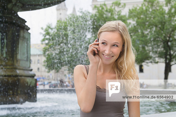 Junge Frau am Telefon vor der Ludwig-Maximilians-Universität lächelnd