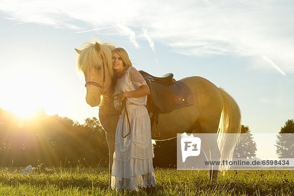 Lächelnde Frau in weißem Kleid mit Pferd auf einer Wiese
