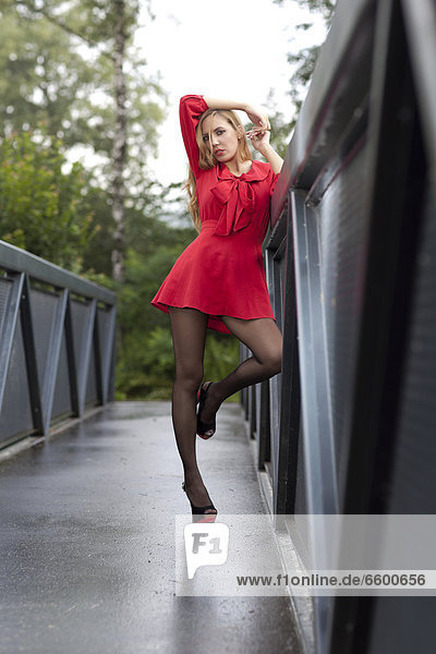 Young woman in a short red dress and high heels posing on a bridge