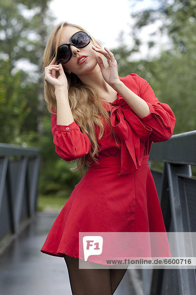 Young woman with sunglasses in a short red dress posing on a bridge