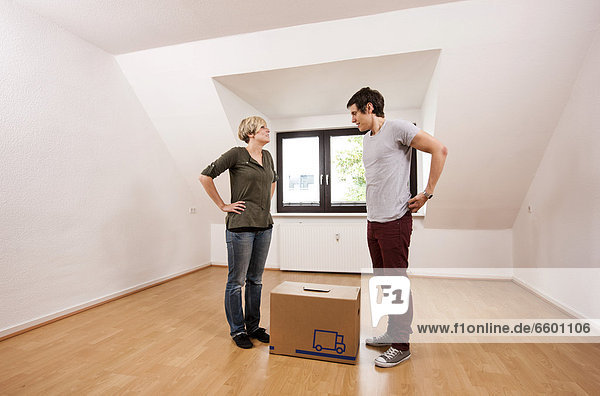 Young couple carrying the first moving box into the empty living room in a new apartment