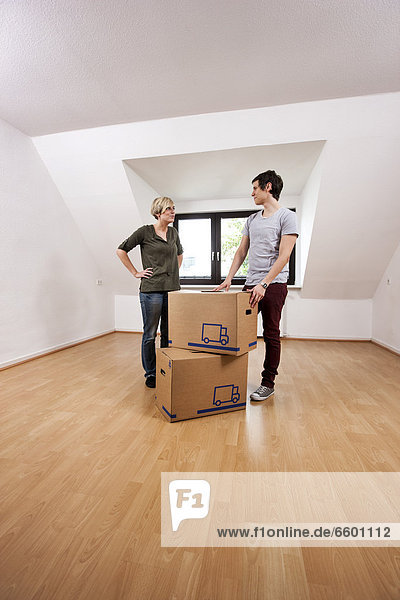 Young couple carrying the first moving boxes into the empty living room in a new apartment