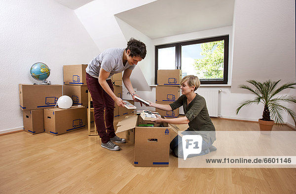 Young couple in an empty room in a new apartment unpacking the first boxes