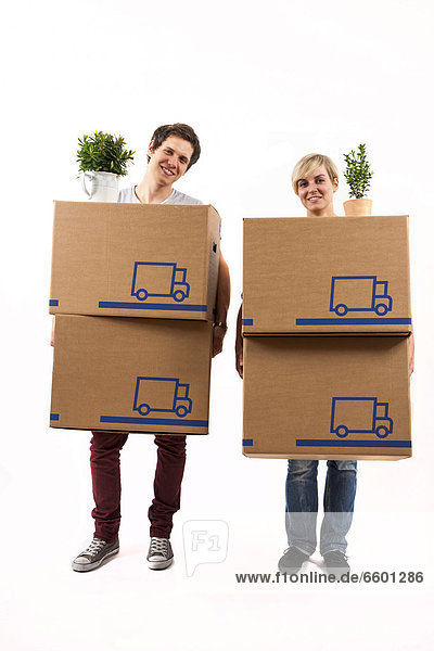 Young couple carrying moving boxes and house plants