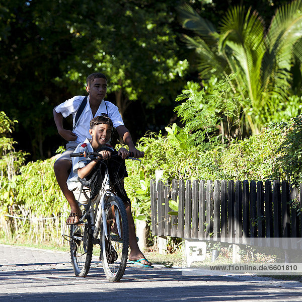 Zwei Jungen in Schuluniform auf einem Fahrrad auf dem Weg zur Schule  Insel La Digue  Seychellen  Afrika  Indischer Ozean