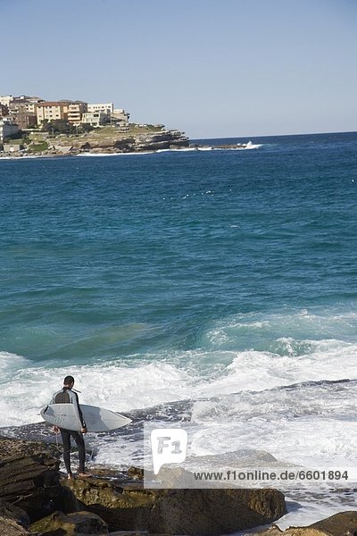 Male Surfer Standing On Rocks At Bondi Beach