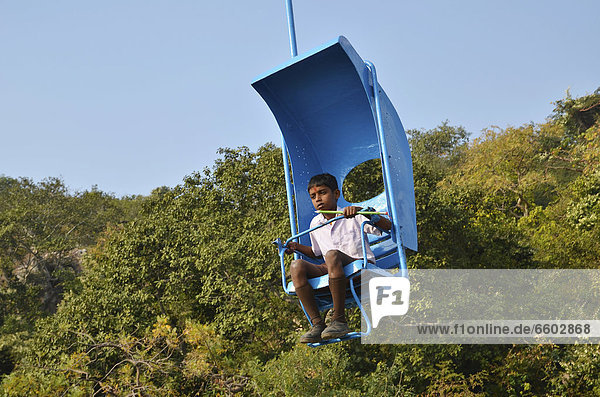 Cable car  chairlift  Indian holding a large pen sitting in a brightly painted one-person chairlift at Vulture Peak  Buddhist pilgrimage destination  Ragir  Rajgir  Rajagrihain  Sanskrit Rajagaha  Pali  Bihar  India  Asia