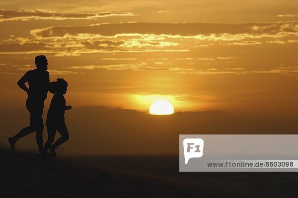 Father And Son Running On Sand Dunes At Sunset
