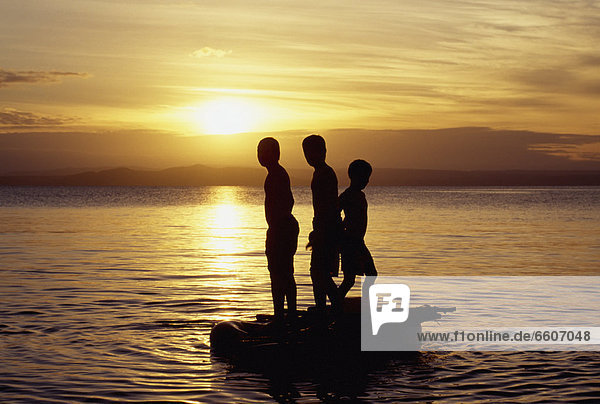 Silhouette Of Young Boys On Boat At Sunset