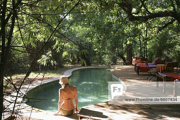 Woman Sitting On The Edge Of Swimming Pool In Jungle