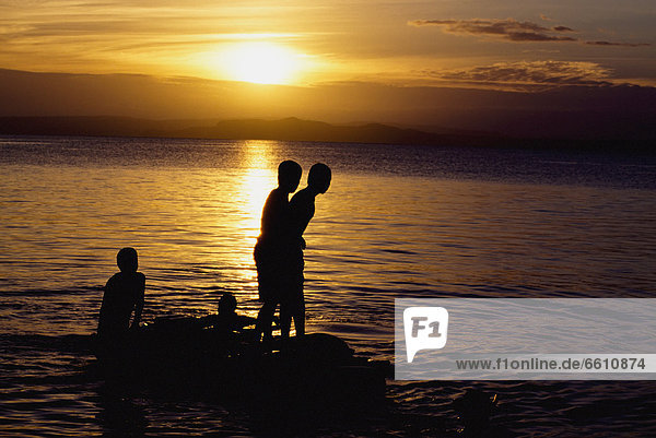 Silhouettes Of Boys On Rocks At Lake Taupo At Sunset