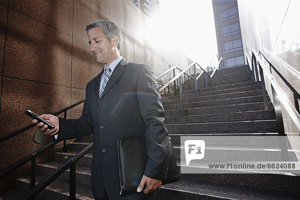 Hispanic businessman text messaging on steps