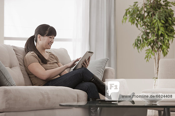 Asian woman sitting on sofa using digital tablet