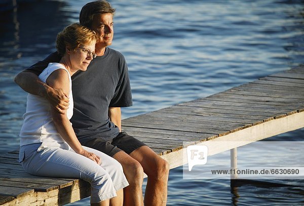 A Couple Sitting On A Dock On The Water