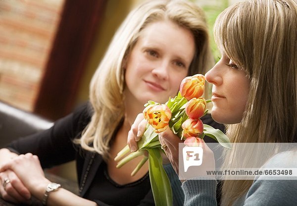 A Woman Smelling Flowers With Another Woman Watching
