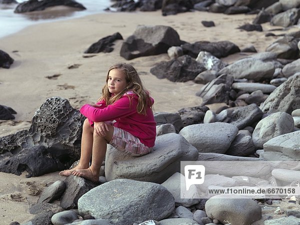 Young Girl Sitting On Some Rocks Near The Water