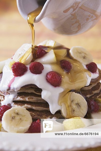 Stack Of Pancakes With Banana  Raspberries  Pear And Syrup Being Poured On