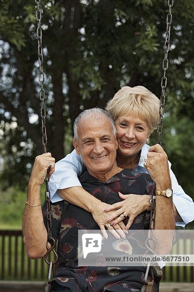 A Man And Woman With The Man Sitting On A Swing