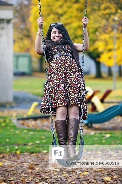 A Young Woman Standing On A Swing At A Playground In Autumn
