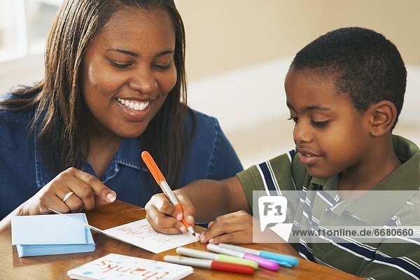 A Boy Writing Thank You Cards With His Mother Watching