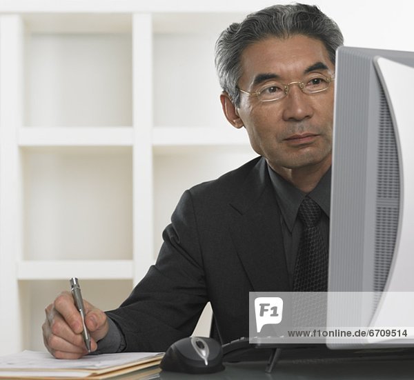 Senior Asian businessman looking at computer and writing