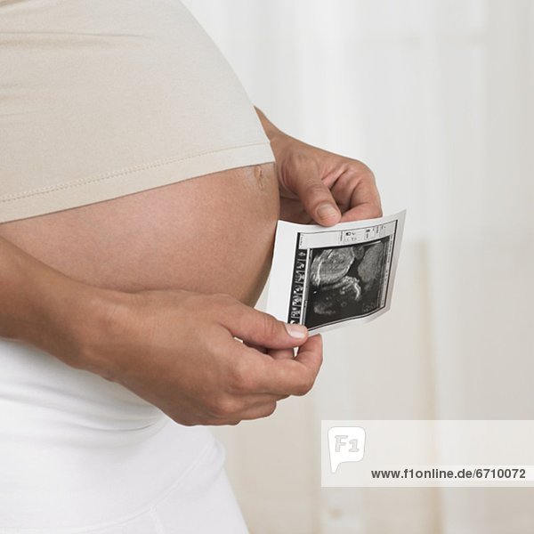 Pregnant woman holding ultrasound next to stomach