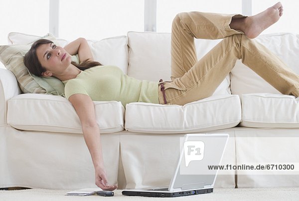 Woman laying on sofa with laptop on floor