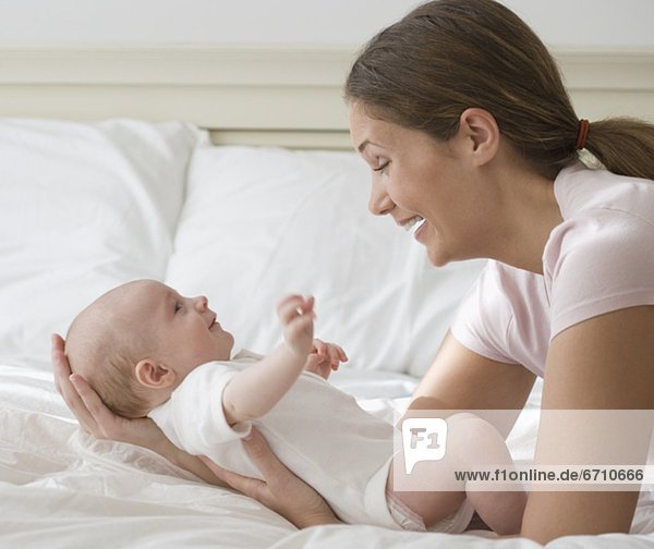 Mother smiling at baby on bed