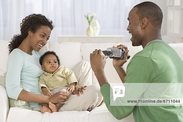 Father video recording mother and baby on sofa