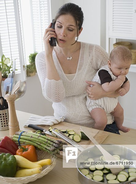 Mother holding baby  talking on telephone and cooking