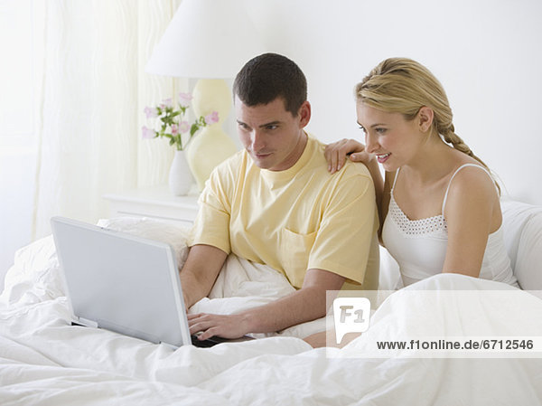Couple looking at laptop in bed