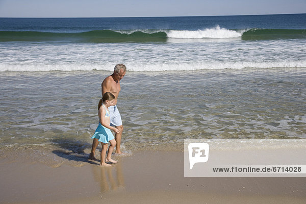 Father and daughter walking in ocean surf