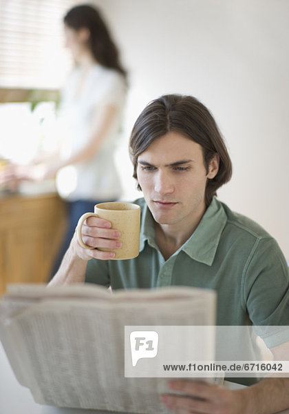 Junger Mann liest Zeitung vor Sofas  Blick zur Kamera