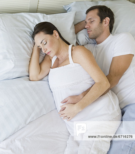 Pregnant Hispanic couple sleeping in bed