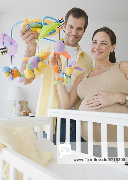 Pregnant Hispanic couple holding mobile over crib