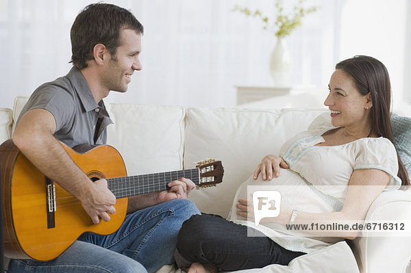 Hispanic man playing guitar for pregnant wife