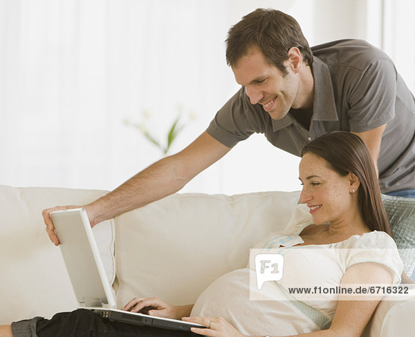 Pregnant Hispanic couple looking at laptop
