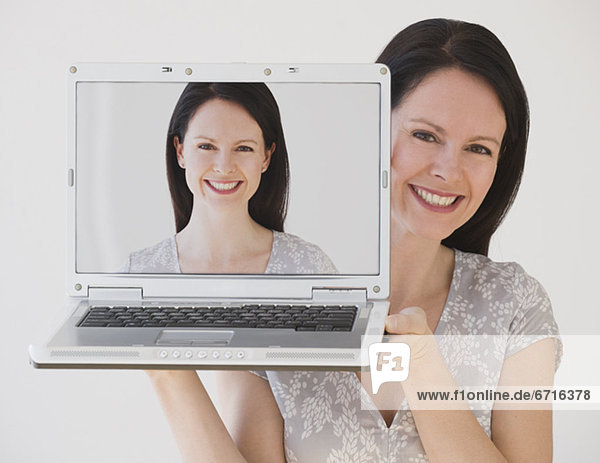 Woman holding laptop next to face