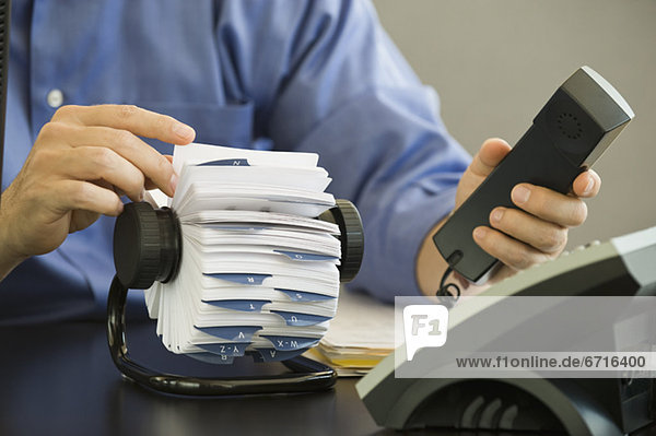 Businessman holding telephone and looking at card file