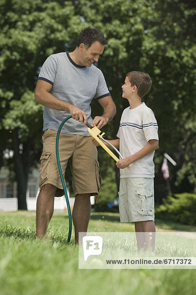 Boy helping father with sprinkler in backyard