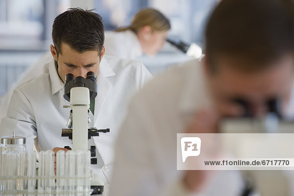 Scientists using microscopes in pharmaceutical laboratory
