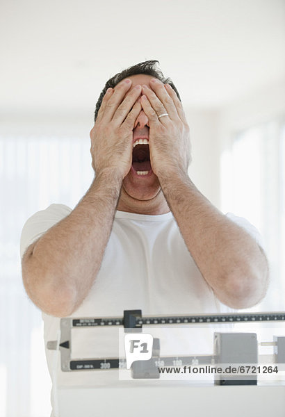 Mature man on scales screaming and covering his eyes